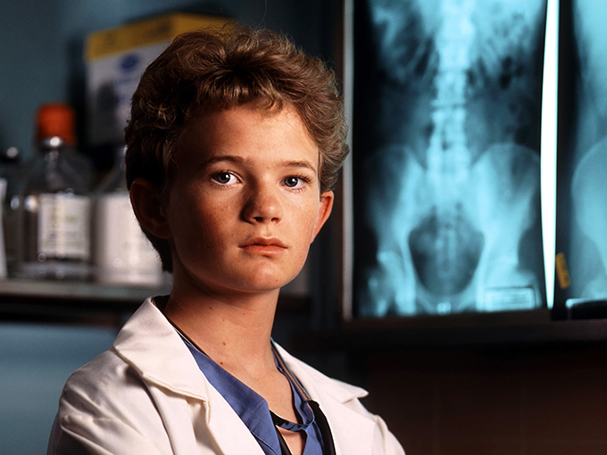 Young Doogie Howser in a white lab coat in front of X-ray light boxes